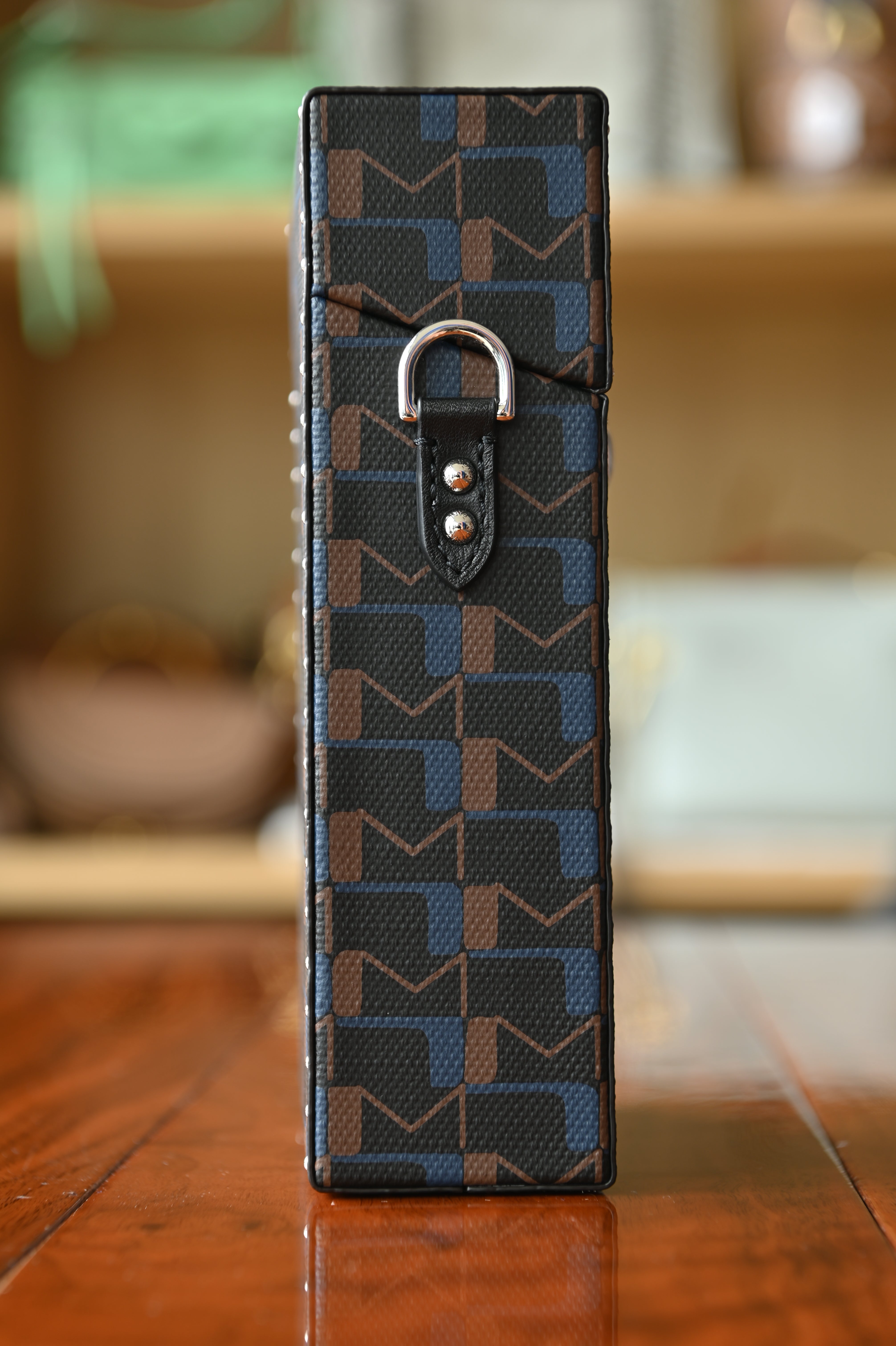 Moynat Patterned black and blue leather wallet with a silver buckle on a wooden surface.