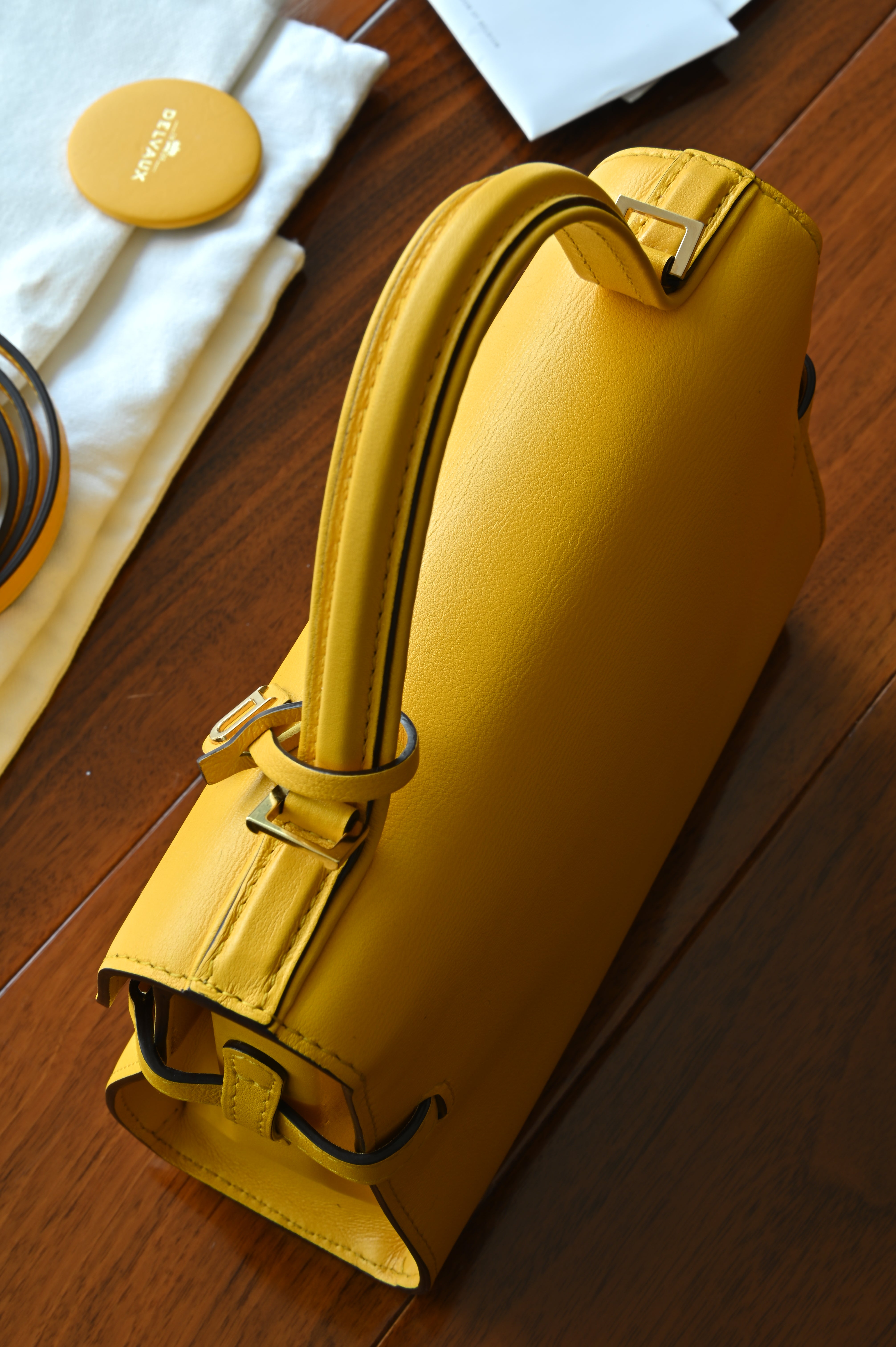 Close-up of the authentic Delvaux Tempête Mini Souple Safra Yellow Leather Top Handle Bag highlighting the leather base, side construction and premium stitching.