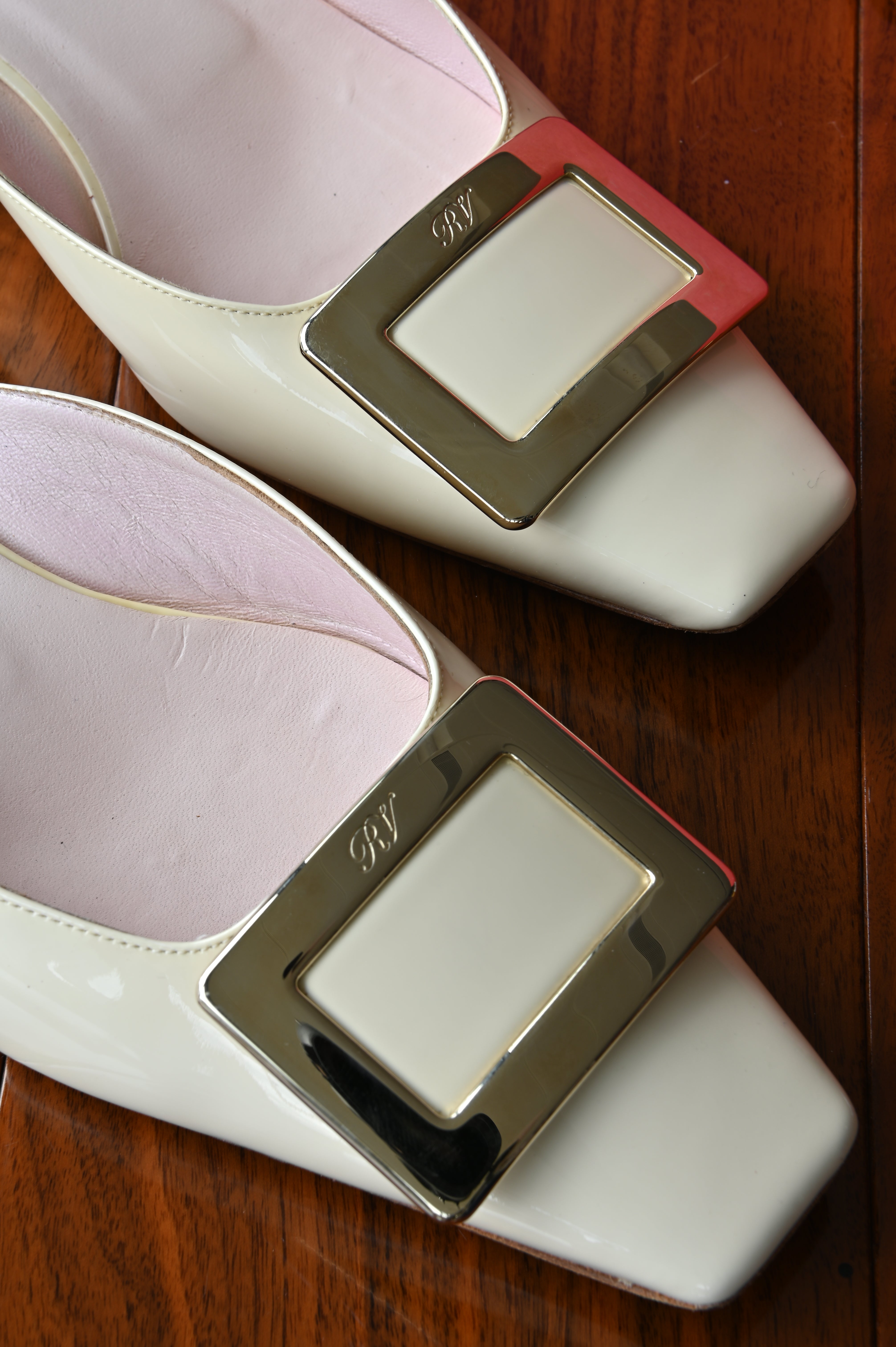 Close-up of the polished signature Roger Vivier oversized buckle on glossy ivory patent leather mules.
