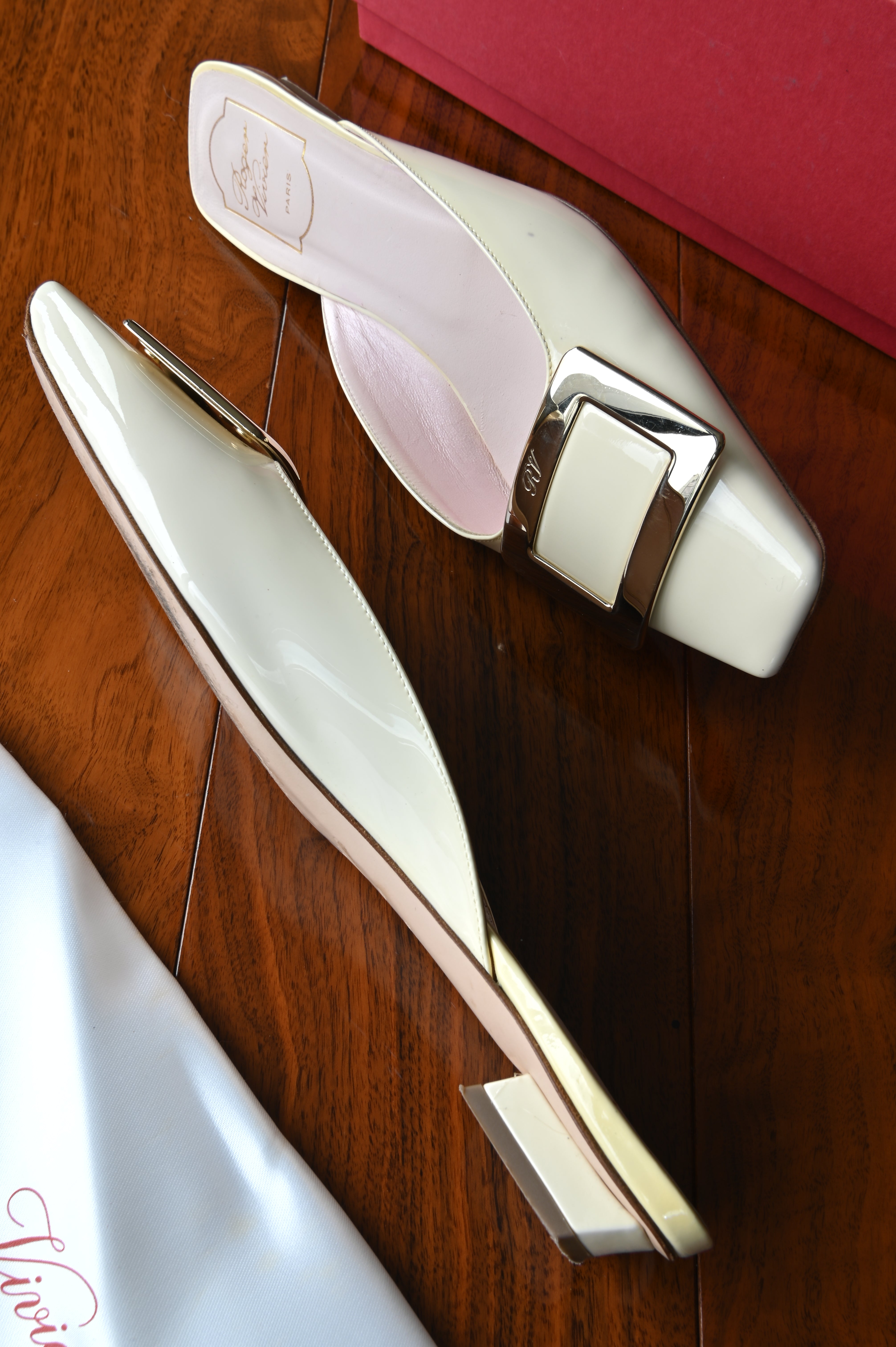 Elegant side view of authentic Roger Vivier Belle Vivier ivory patent leather mules featuring the sleek silhouette and signature buckle.