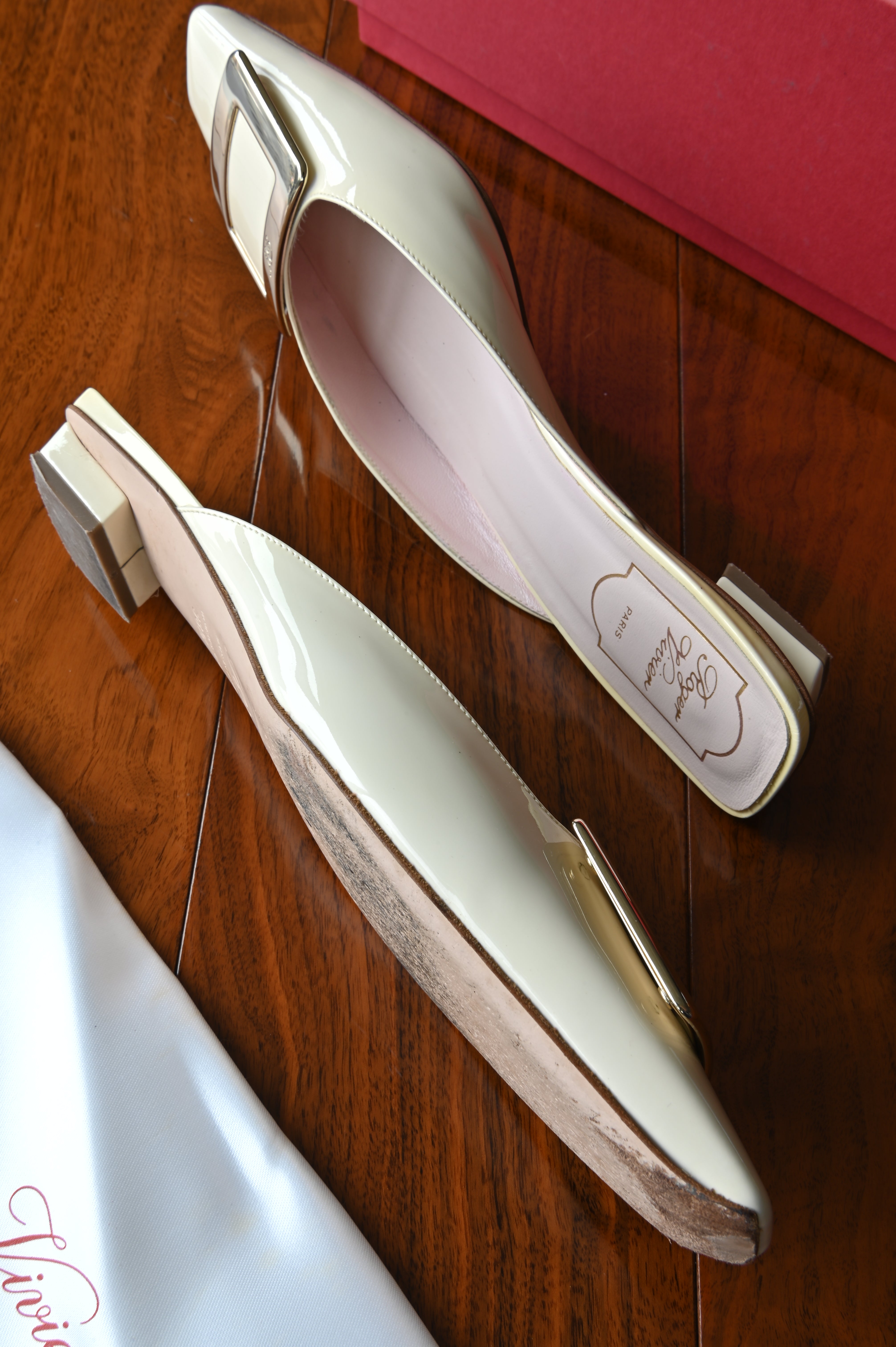 Top angled view of authentic Roger Vivier Belle Vivier ivory patent leather mules showcasing the blush pink leather footbeds and iconic buckle.