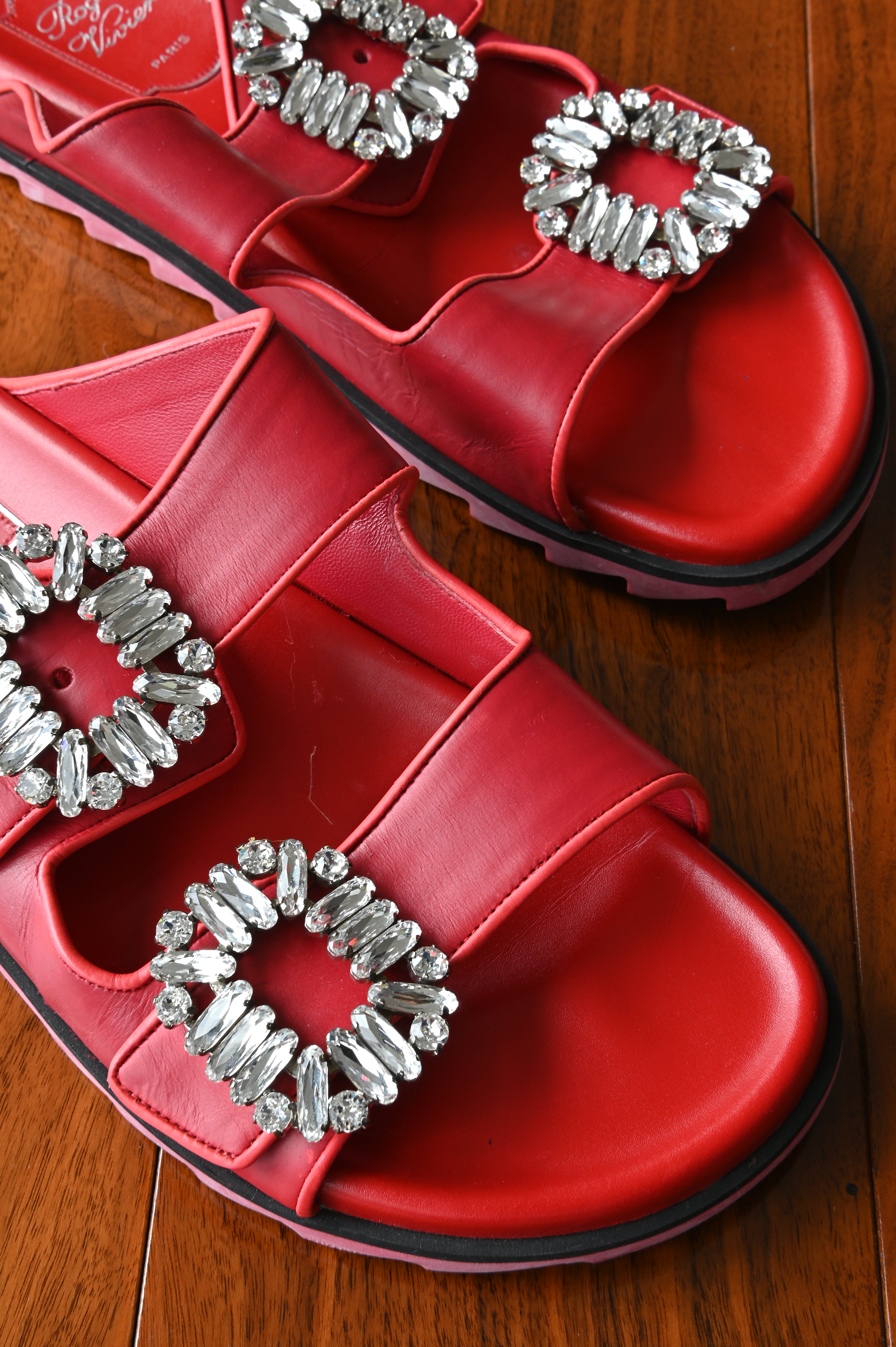 Close-up of the Roger Vivier signature crystal strass buckles on smooth red leather double straps.