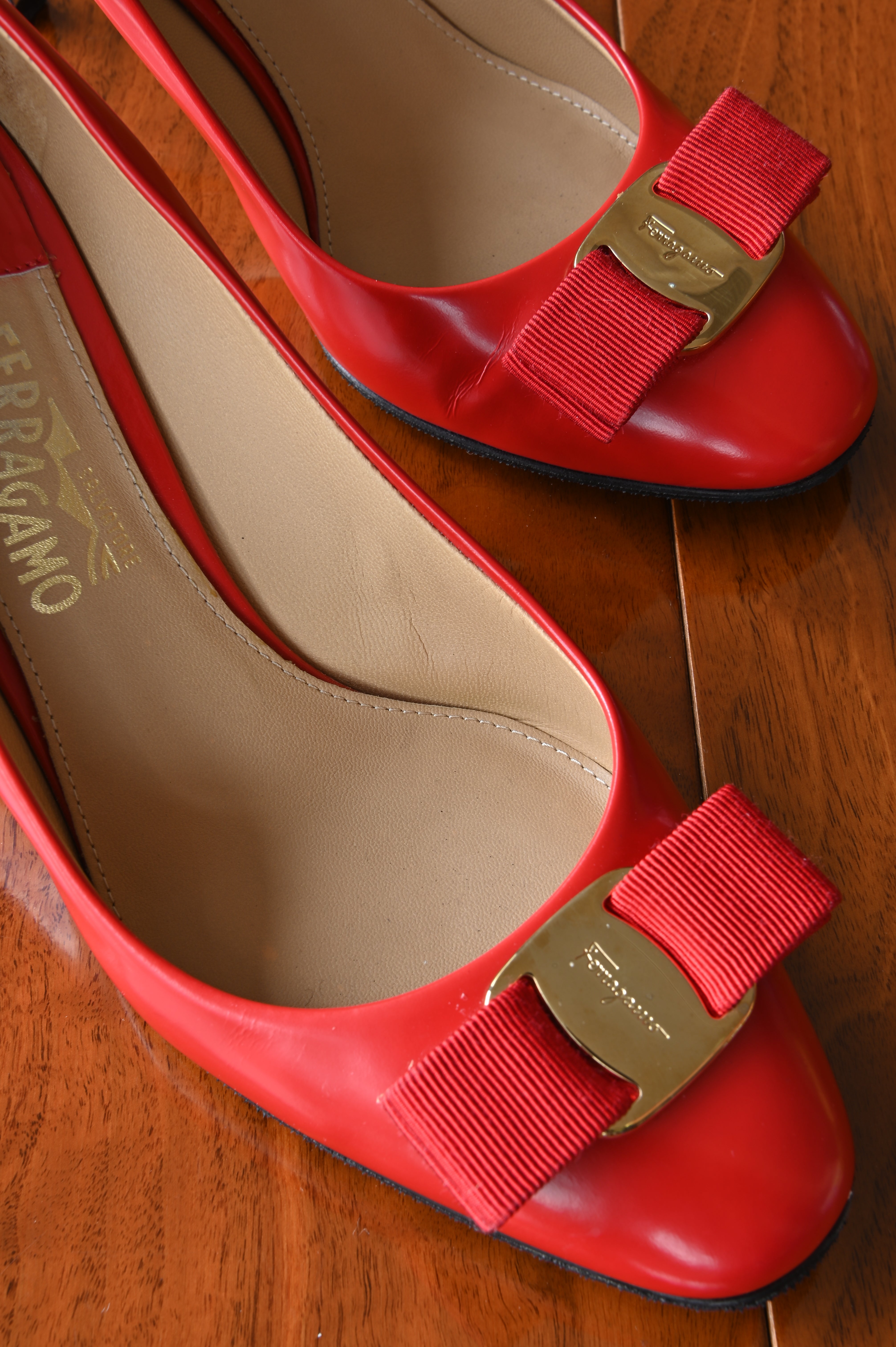 Close-up of the iconic Salvatore Ferragamo Vara grosgrain bow with gold-tone logo plaque on smooth red leather.