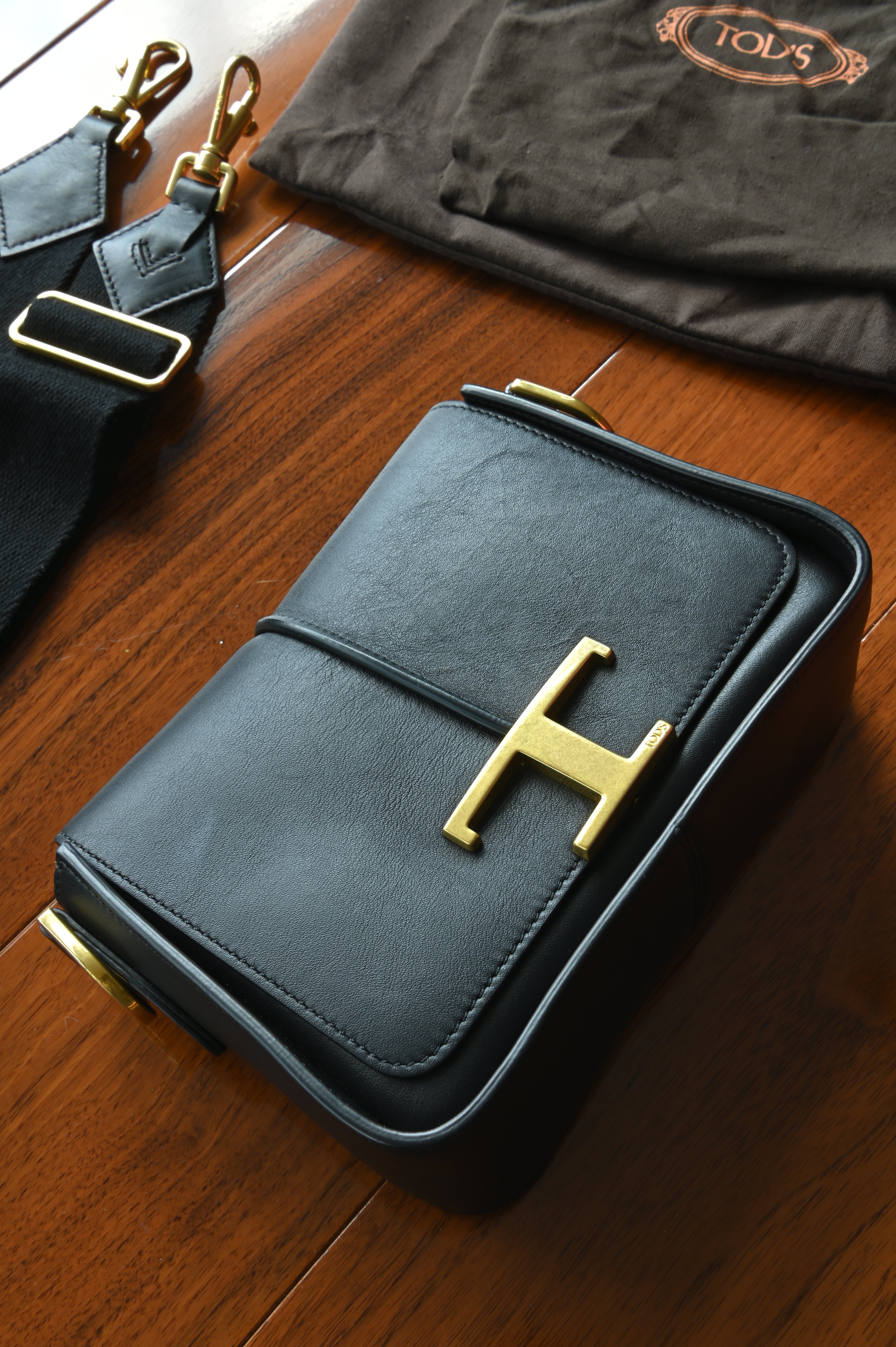 Authentic Tod’s Black Lamb Leather Logo Crossbody Bag featuring the signature oversized gold-tone T logo, front view.