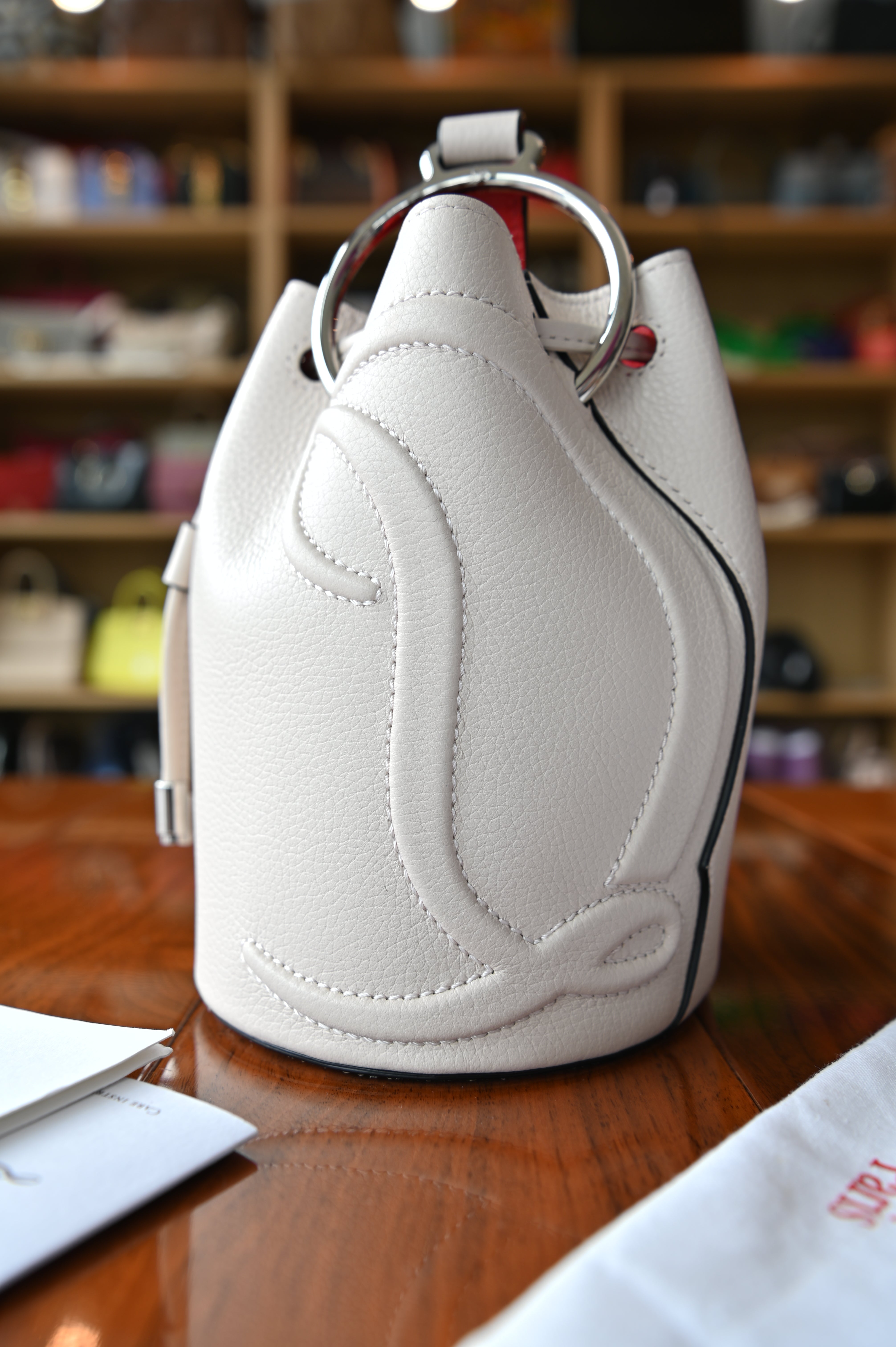 Authentic Christian Louboutin By My Side Bucket Bag showing the oversized CL motif and silver-tone ring hardware on the side.