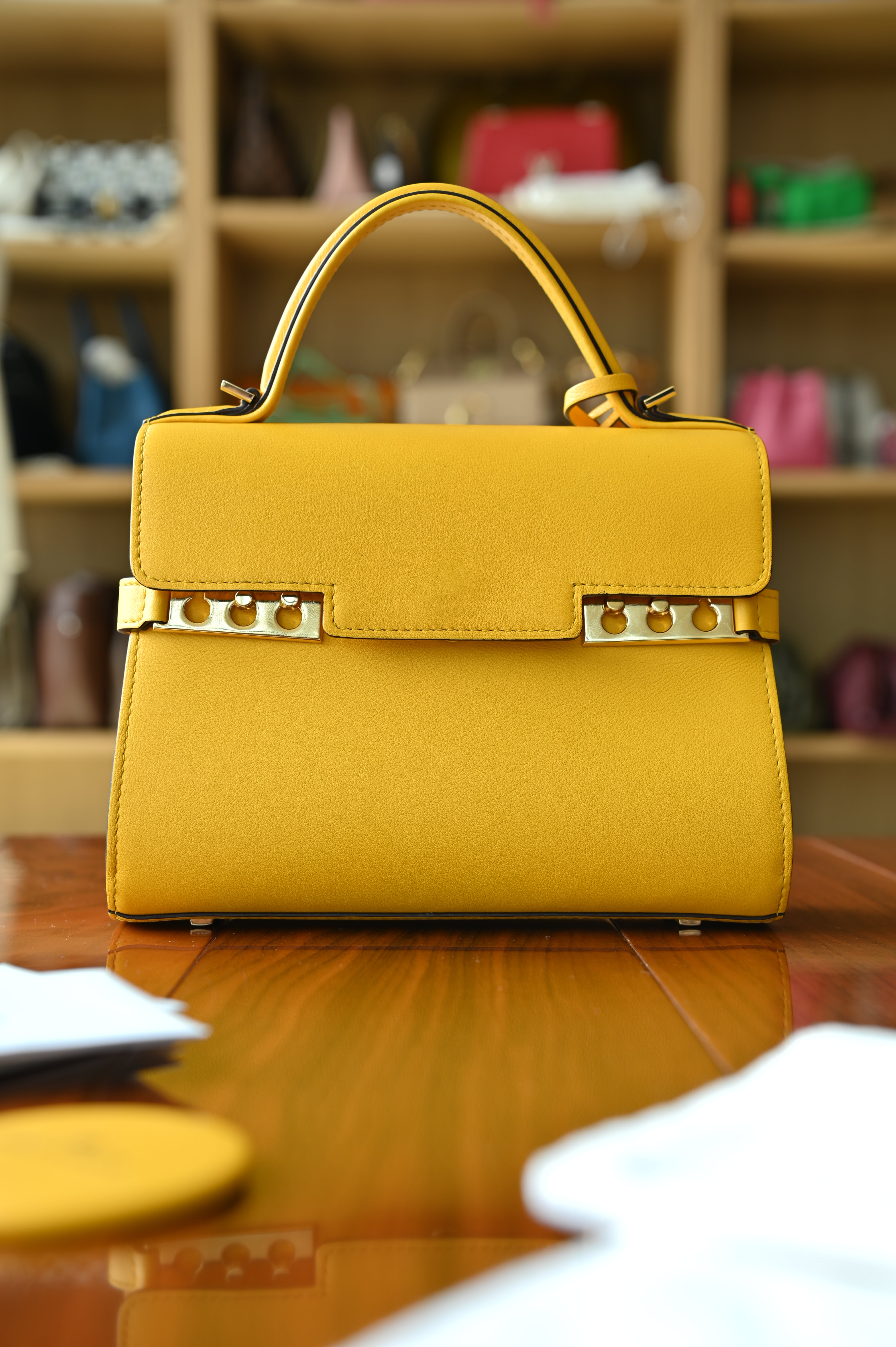 Authentic Delvaux Tempête Mini Souple Safra Yellow Leather Top Handle Bag featuring the signature Tempête buckle, structured silhouette and top handle, front view.