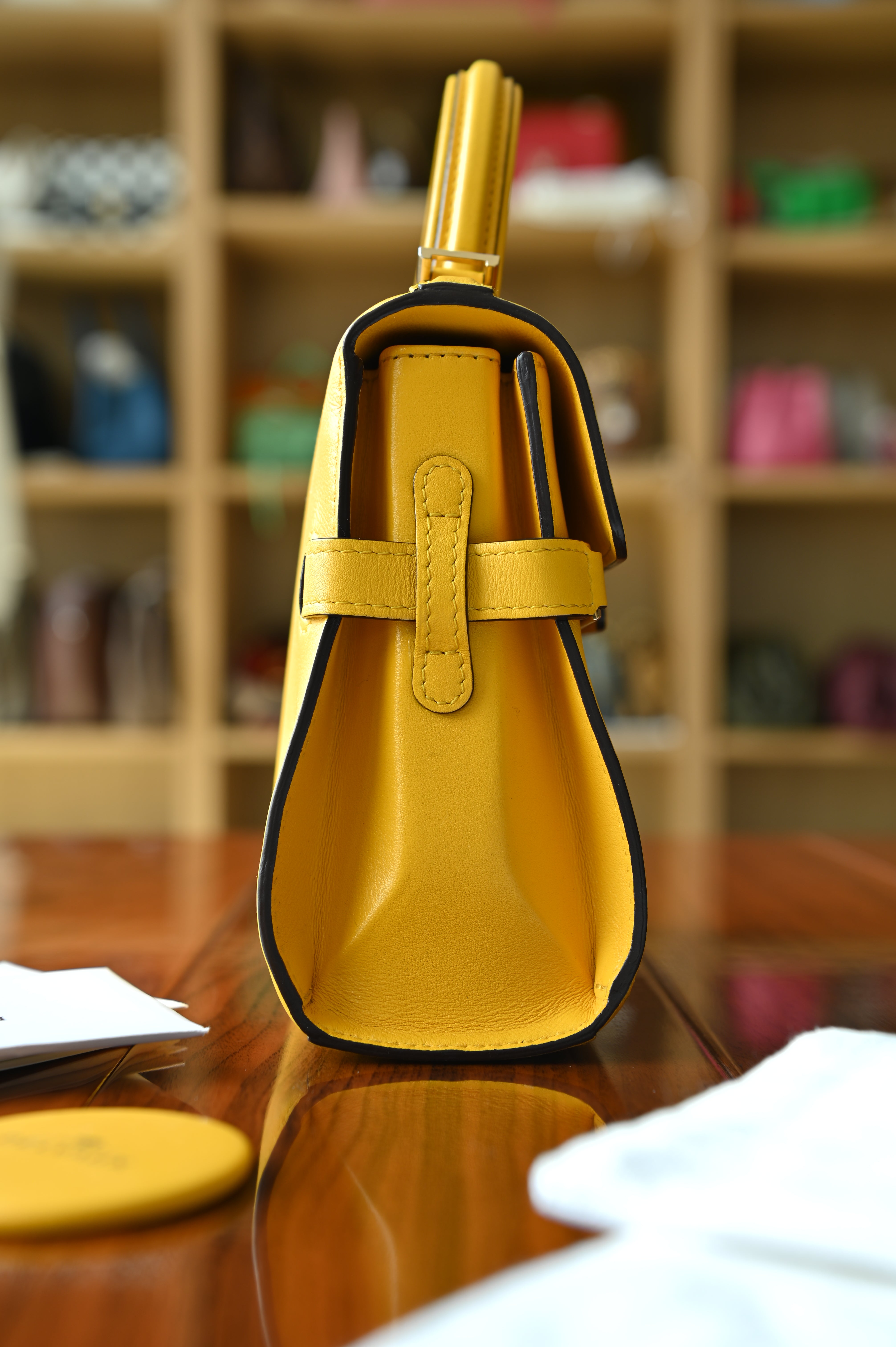 Authentic Delvaux Tempête Mini Souple Safra Yellow Leather Top Handle Bag showing the left side profile with structured gussets and top handle.