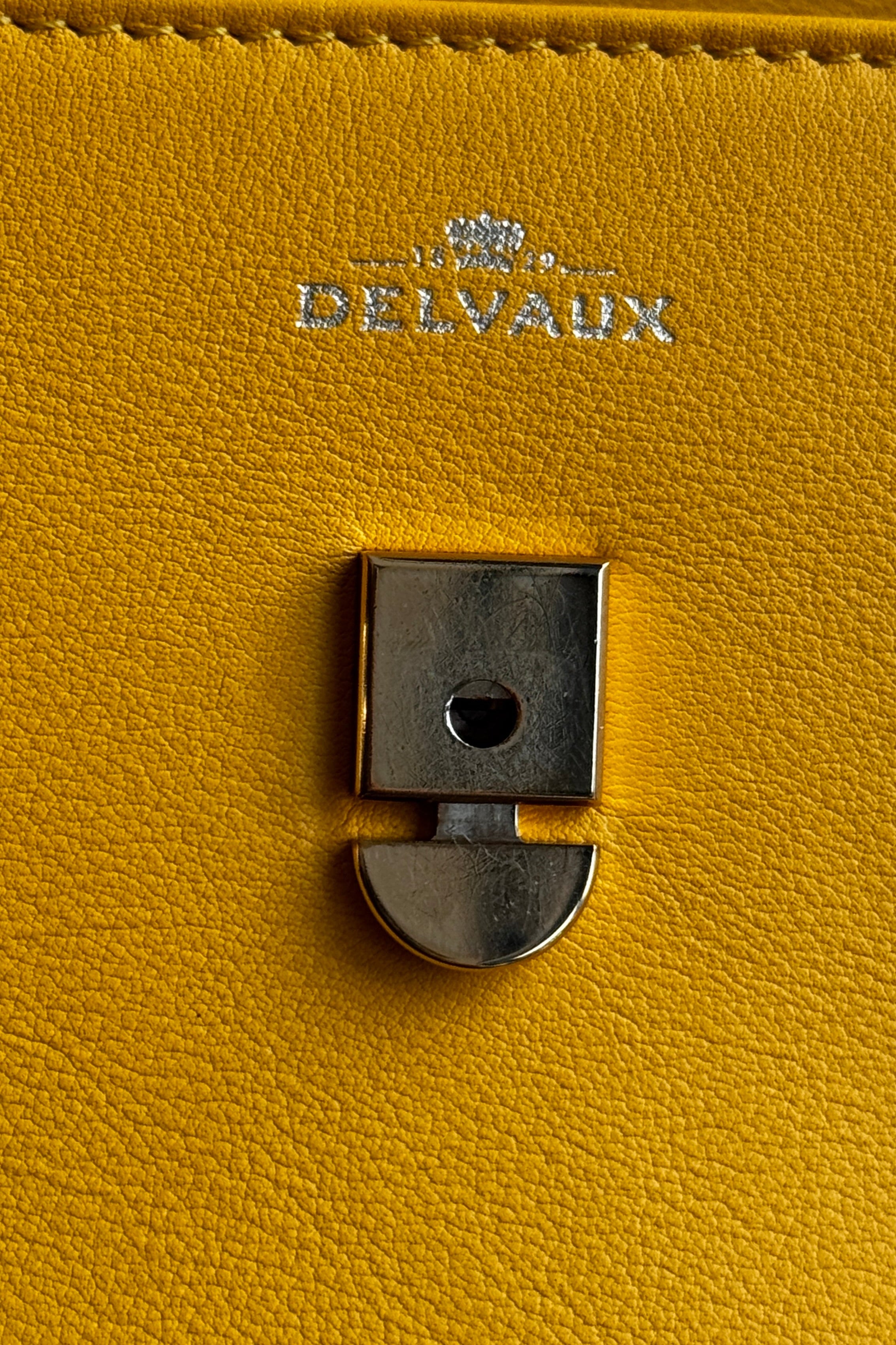 Close-up of the authentic Delvaux Tempête Mini Souple Safra Yellow Leather Top Handle Bag highlighting the iconic Tempête clasp and premium hardware.