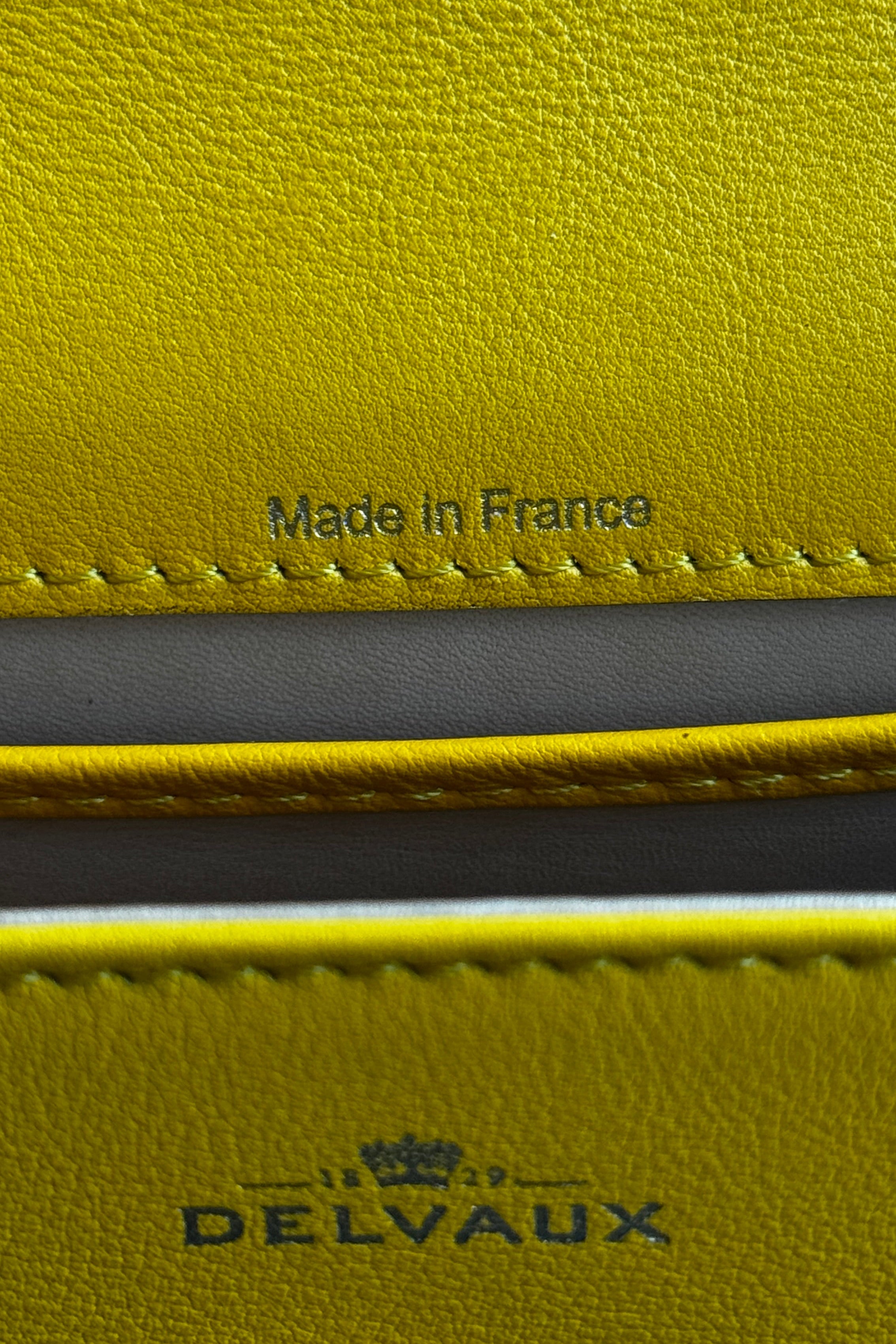 Close-up of the authentic Delvaux Tempête Mini Souple Safra Yellow Leather Top Handle Bag showcasing the embossed Delvaux logo on the leather exterior.
