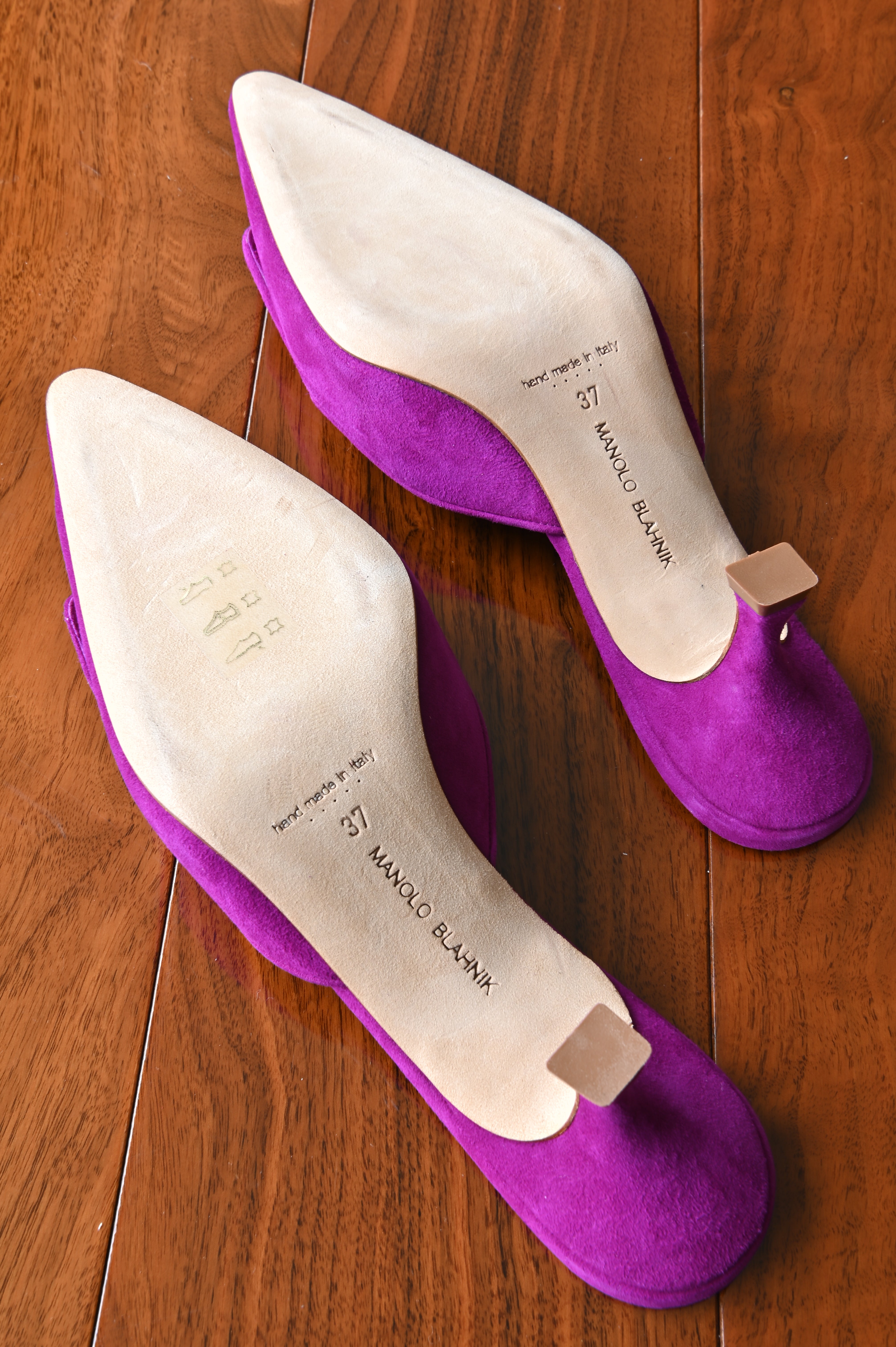 Bottom view of authentic Manolo Blahnik purple suede buckle mules displaying the clean leather outsoles, Made in Italy stamp, and size 37 markings