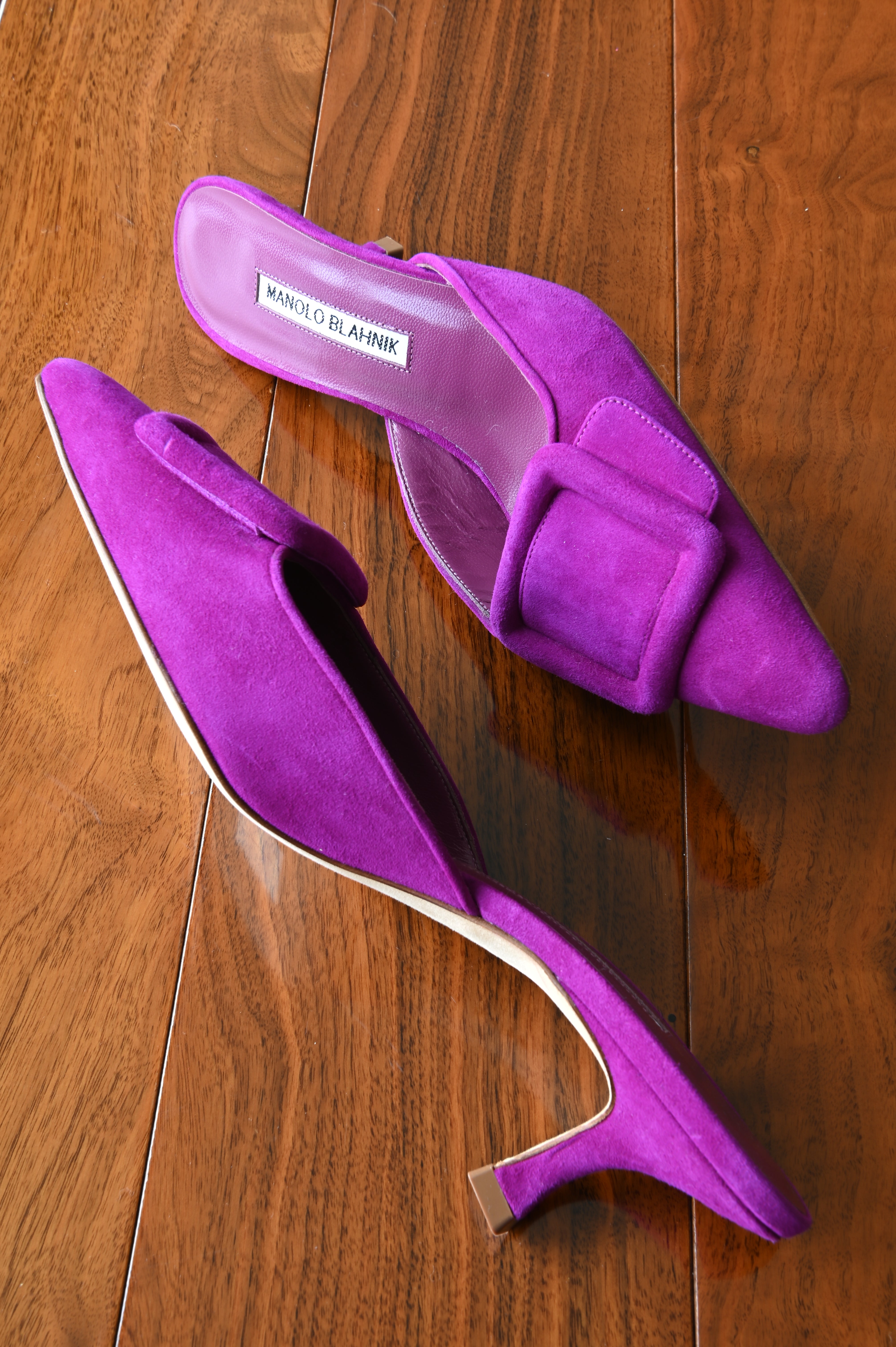 Angled side view of authentic Manolo Blahnik purple suede buckle mules showcasing the sleek pointed toe, oversized buckle, and elegant kitten heel