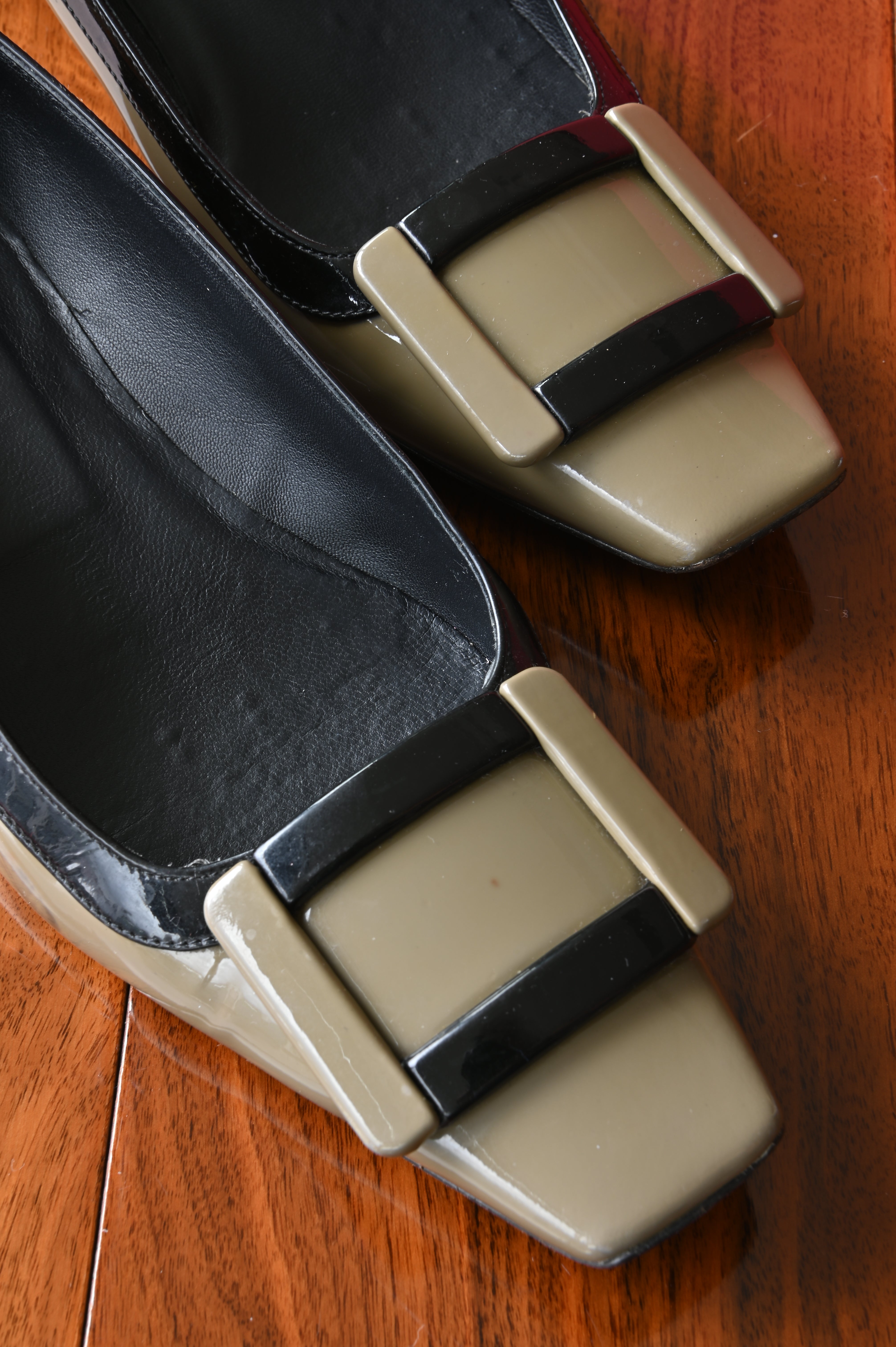 Close-up of the signature oversized Roger Vivier buckle on taupe patent leather with contrasting black trim.
