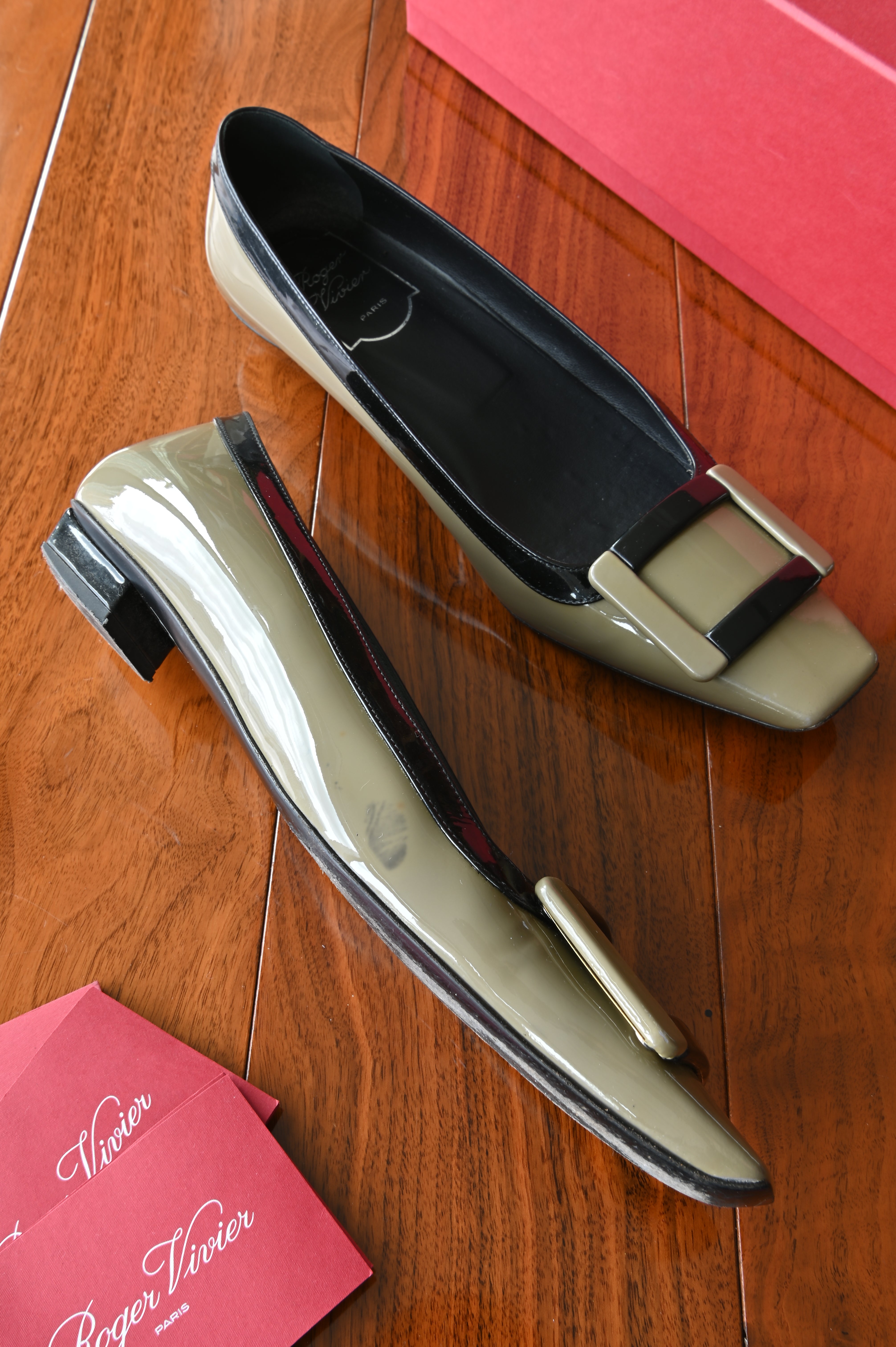 Side profile of authentic Roger Vivier Belle Vivier patent leather pumps highlighting the glossy taupe finish, black trim, and low block heel.