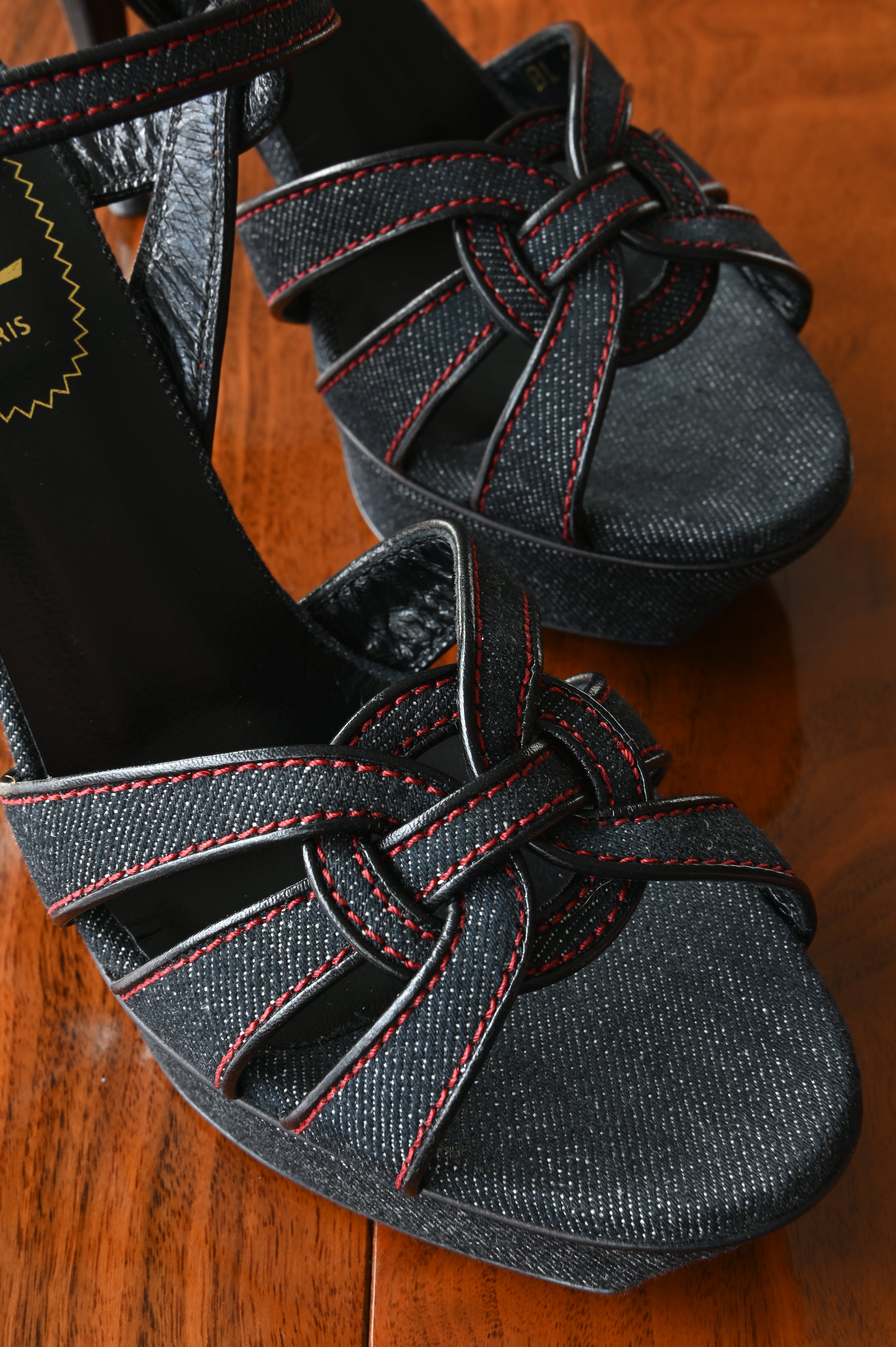 Close-up of the signature interwoven Tribute front straps in textured black denim with contrasting red stitching