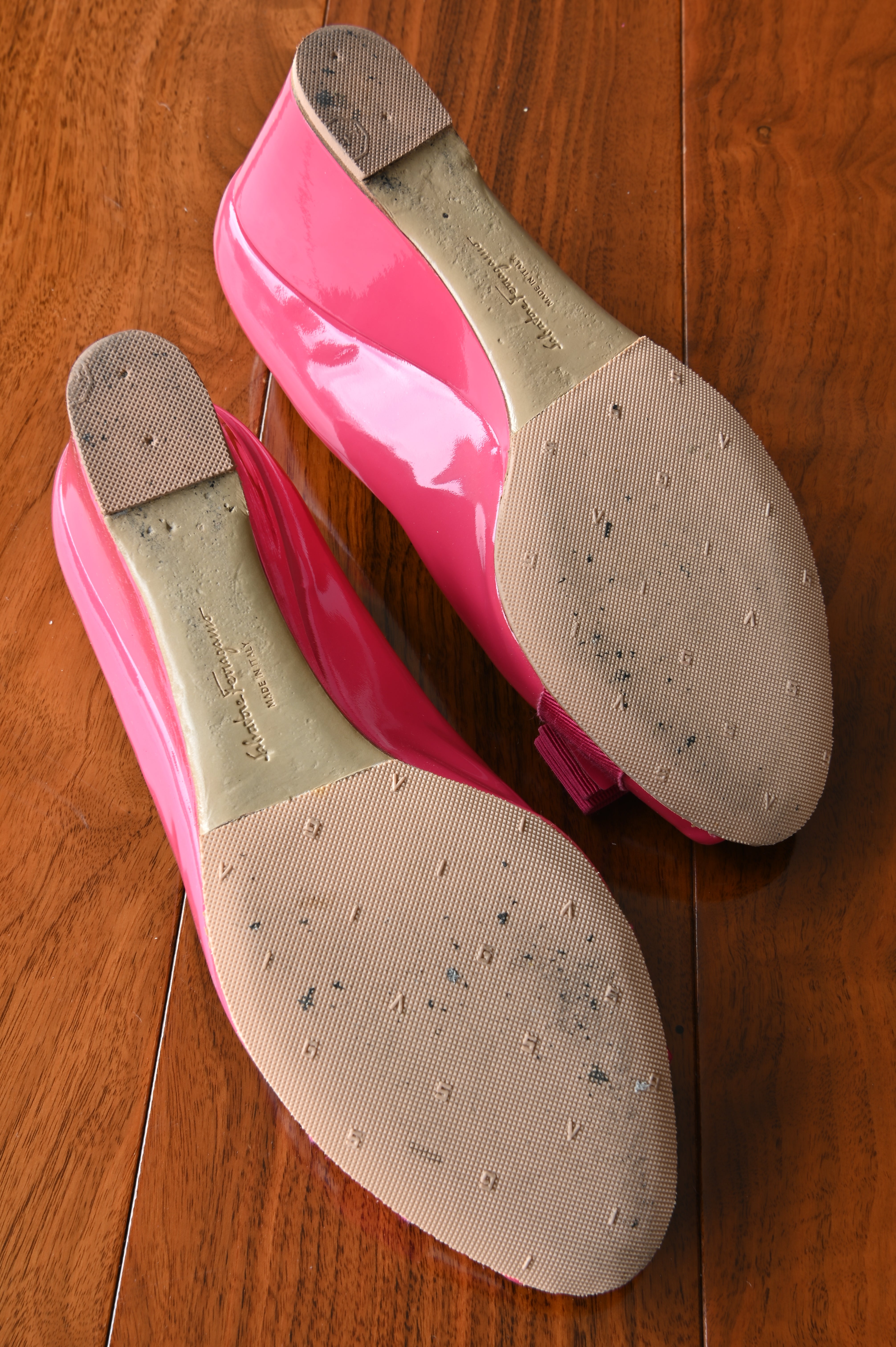 Bottom view of authentic Salvatore Ferragamo pink patent leather Vara Bow Wedge Pumps displaying the leather and rubber outsoles with light signs of wear.