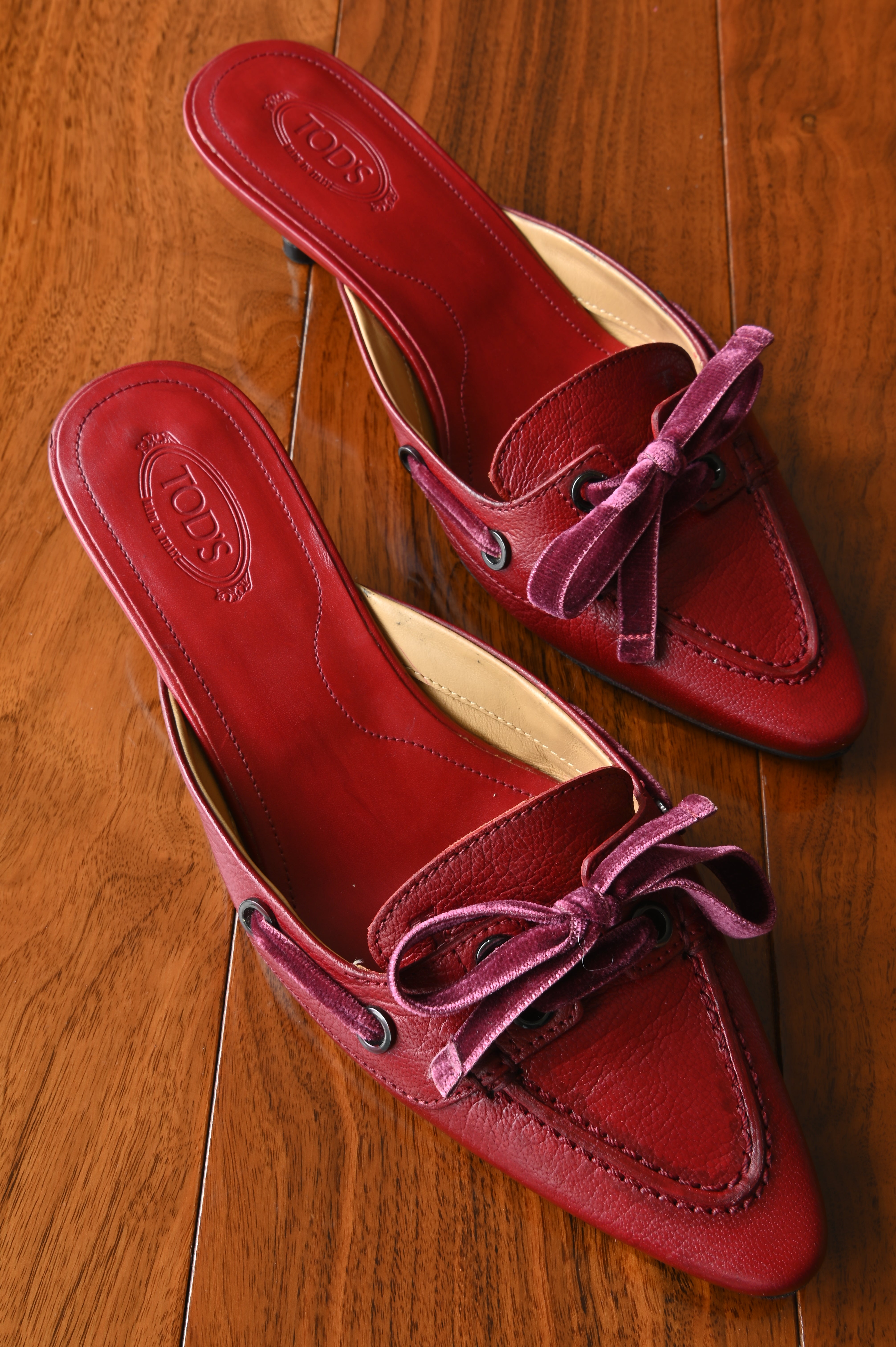Authentic Tod’s burgundy leather kitten heel mules featuring elegant velvet bow detailing, pointed toe, and comfortable 2-inch heels.